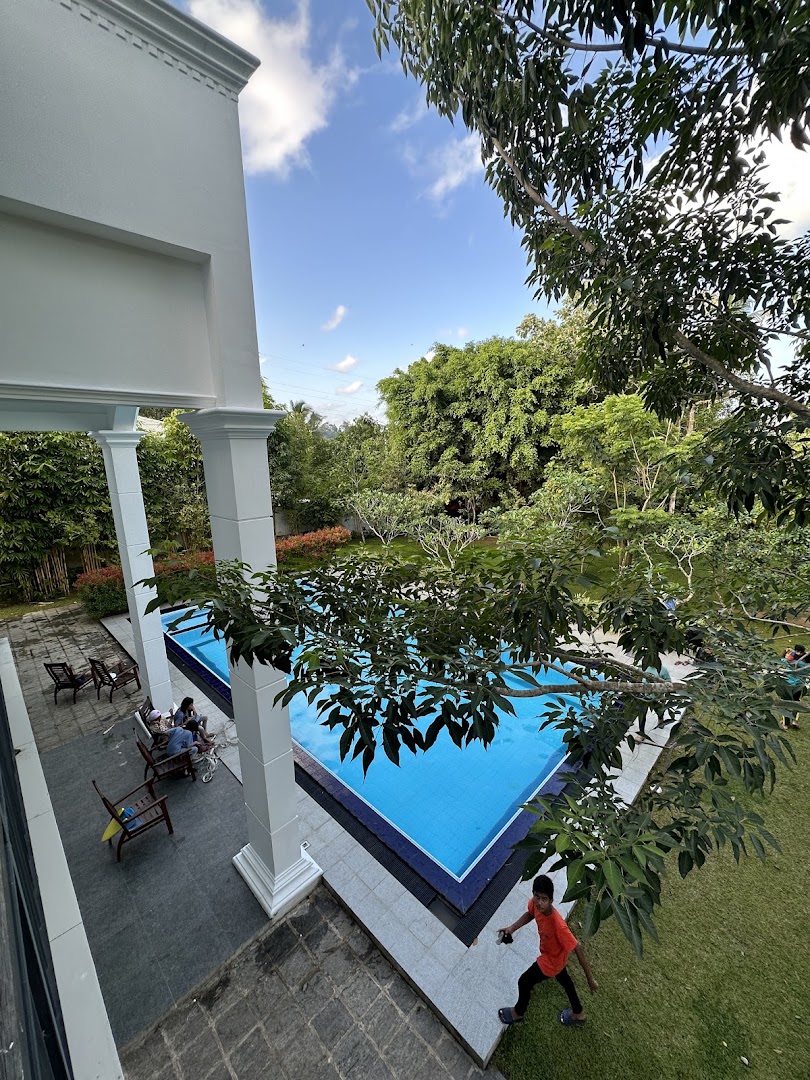Blue swimming pool surrounded by greenery and white villa columns